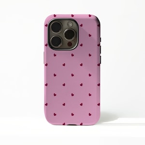 May include: A pink phone case with a repeating pattern of small, dark red hearts. The case has a glossy finish and a camera cutout on the back. The phone case is designed to fit a smartphone.