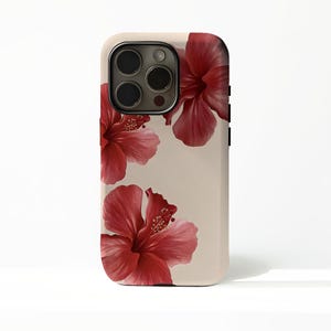 May include: A phone case with a beige backdrop, adorned with three large, detailed red hibiscus flowers. The case includes a black camera lens and side buttons. The floral design brings a touch of nature and elegance to the phone accessory.