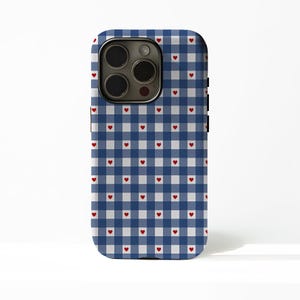 Puede incluir: Una funda de teléfono con un patrón de cuadros azul y blanco, adornada con pequeños corazones rojos. La funda tiene un recorte para la cámara y botones laterales negros.