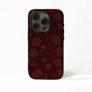 May include: A burgundy phone case with a floral peony and leaf pattern. The case has a glossy finish and a camera cutout. The design is a repeating pattern of dark red flowers and foliage.