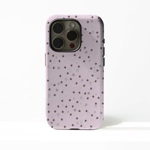 May include: A lavender phone case with a repeating pattern of brown stars, silver snowflakes, and swirls. The case has a camera cutout and black side buttons. The phone case is designed to protect the phone from damage.