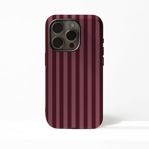 Puede incluir: Funda de teléfono a rayas burdeos y granate. La funda tiene un acabado brillante y un recorte para la cámara. Las rayas verticales están espaciadas uniformemente, creando un diseño simple y elegante.