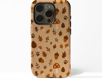 May include: A tan phone case with a repeating pattern of brown leaves, acorns, mushrooms, paw prints, and pinecones. The case has a black border and a camera cutout. The design evokes an autumn theme.