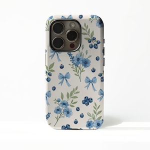 May include: A phone case with a white background and a repeating pattern of blue flowers, bows, blueberries, and green leaves. The case has a camera cutout and black side buttons.