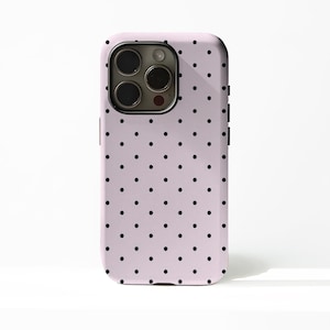 May include: A pale pink phone case featuring a pattern of black polka dots. The case has a camera aperture and black side buttons. The phone case is designed to fit a smartphone.