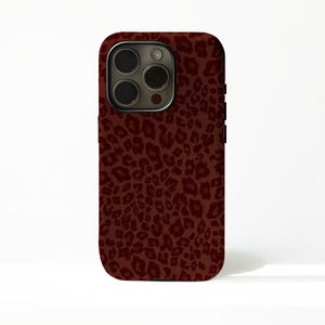 Könnte beinhalten: Eine kastanienbraune Handyhülle mit Leopardenmuster. Die Hülle hat eine dunkle Kameralinse und eine schwarze Seitentaste. Der Leopardenprint ist ein sich wiederholendes Muster aus dunkelbraunen Flecken auf kastanienbraunem Hintergrund.