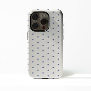 May include: A white phone case with a pattern of evenly spaced blue polka dots. The case has a black camera module and black side buttons. The phone case is designed to fit a smartphone.
