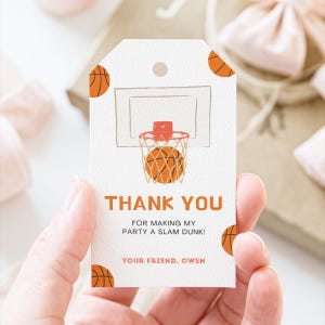 May include: White gift tag with a basketball theme. The tag features a basketball net and ball illustration, with the words "THANK YOU" in orange. The text "FOR MAKING MY PARTY A SLAM DUNK!" and "YOUR FRIEND, OWEN" are also included.