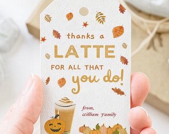 May include: A white gift tag with fall-themed illustrations and text. The tag reads "thanks a LATTE for all that you do!" with a latte, pumpkin, and pumpkins. The tag is held by a person.