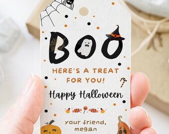 Può includere: Un'etichetta regalo bianca di Halloween con la parola "BOO" in nero, con un fantasma, un ragno e un cappello da strega. L'etichetta recita "Ecco un dolcetto per te! Buon Halloween" con un design di zucca e caramelle.