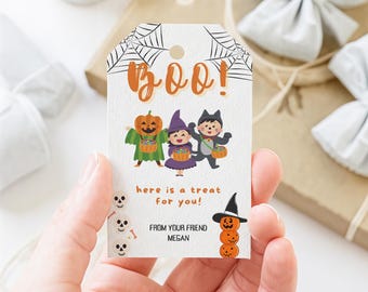 以下が含まれることがあります： オレンジ色の筆記体で「BOO！」と書かれたハロウィーンをテーマにしたギフトタグ。タグには、バスケットを持っている3人のトリックオアトリーター、カボチャ、魔女、猫のイラストが描かれています。「here is a treat for you！」というテキストも含まれています。