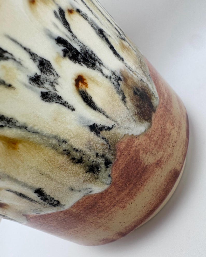 Puede incluir: Primer plano de un jarr&oacute;n de cer&aacute;mica con un dise&ntilde;o veteado &uacute;nico. El jarr&oacute;n presenta una base de color crema con vetas negras, marrones y beige. La parte inferior del jarr&oacute;n tiene una banda marr&oacute;n rojiza. El dise&ntilde;o le da al jarr&oacute;n un aspecto natural y org&aacute;nico.