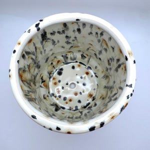 Puede incluir: Maceta de cer&aacute;mica con dise&ntilde;o moteado. El interior y el exterior presentan una base blanca con manchas negras y marrones. La maceta tiene forma redonda con un orificio de drenaje en la base.