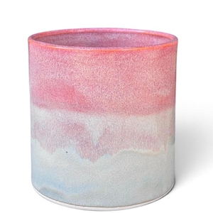 May include: A cylindrical ceramic vessel featuring a smooth gradient glaze that transitions from a vibrant pink at the top rim to a soft, muted light blue at the base. The surface has a subtle, speckled texture throughout the entire exterior.