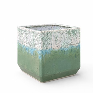 May include: A square ceramic planter featuring a reactive glaze finish. The exterior transitions from a solid sage green base to a vibrant turquoise band, topped with a speckled white rim. The vessel has a wide opening and a flat base.