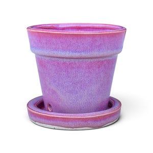 Puede incluir: Una maceta de cerámica cónica con un acabado de esmalte reactivo en tonos magenta y morado. La maceta presenta un borde ancho y un plato circular a juego con un orificio de drenaje visible en el lateral, mostrando una textura lisa.