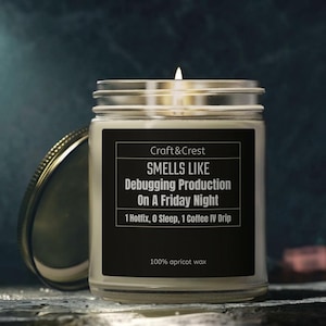 Könnte beinhalten: Eine Kerze im klaren Glas mit brennendem Docht und schwarzem Etikett. Das Etikett trägt die Aufschrift: Craft & Crest, SMELLS LIKE Debugging Production On A Friday Night, 1 Hotfix, 0 Sleep, 1 Coffee IV Drip, 100% apricot wax. Ein Metalldeckel liegt neben dem Glas.