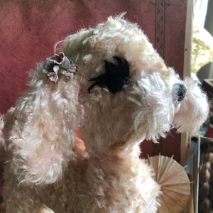 May include: A white plush toy dog with a black eye patch and a small flower embellishment on its ear. The dog is made of soft, fluffy material and has a sweet, innocent expression.