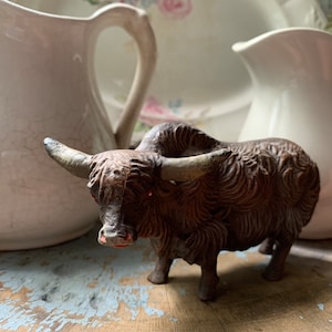 May include: A brown and black yak figurine with horns. The figurine is standing on a wooden surface.