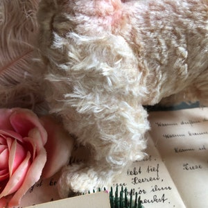 May include: A vintage white plush toy with a soft, fluffy texture. The toy is lying on a piece of paper with handwritten text that reads "Warun driftere de, Warum breur, Narum ist, Liese, lebt tief Herren, h&ouml;r ilmo meukst."