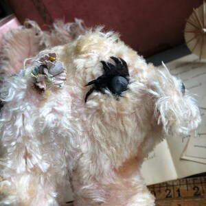 May include: A white plush toy dog with a black eye patch and a floral embellishment on its head. The dog is in a seated position and is looking to the right.
