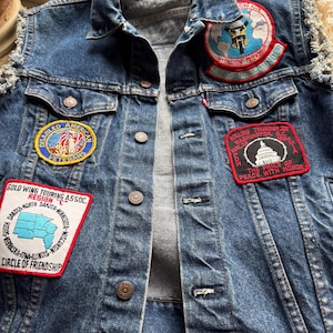 May include: A blue denim vest with several patches sewn on. The patches include a "Disabled American Veterans" patch, a "Gold Wing Touring Assoc. Region C" patch, a "Rolling Thunder 20 Washington D.C. May 25, 1984" patch, and a "Destination Friendship" patch.