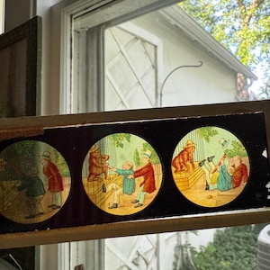 May include: A vintage magic lantern glass slide featuring three circular hand-colored illustrations. The scenes depict a man in a top hat interacting with a caged animal, showing a sequence of events where the man is pulled toward the enclosure.