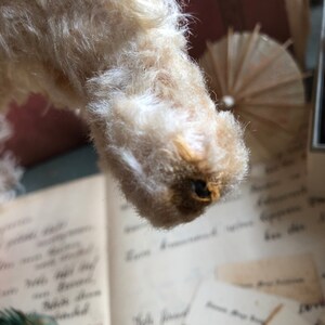 May include: Close-up of a white, fluffy stuffed animal with a brown nose. The animal is upside down and the fur is very soft.