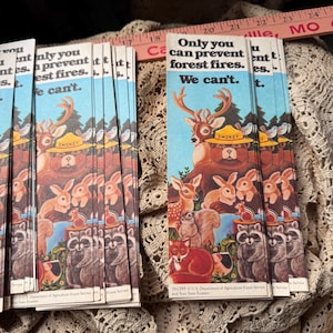 May include: A stack of vintage Smokey Bear bookmarks. Each bookmark features Smokey Bear, a deer, rabbits, and other forest animals. The text reads, "Only you can prevent forest fires. We can't."