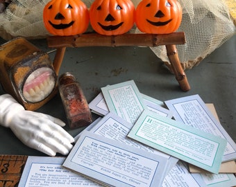 May include: Three orange plastic jack-o'-lanterns with black smiles sit on a small bamboo stand. Other items include a vintage dental mold, a small glass bottle, a white porcelain hand, and several vintage cards with text.