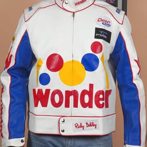 Könnte beinhalten: Weiße Lederjacke mit blauen und roten Akzenten. Auf der Jacke steht das Wort "WONDER" in großen roten Buchstaben, zusammen mit bunten Kreisen und dem Namen "Ricky Bobby". Sie hat einen Reißverschluss und einen Stehkragen.