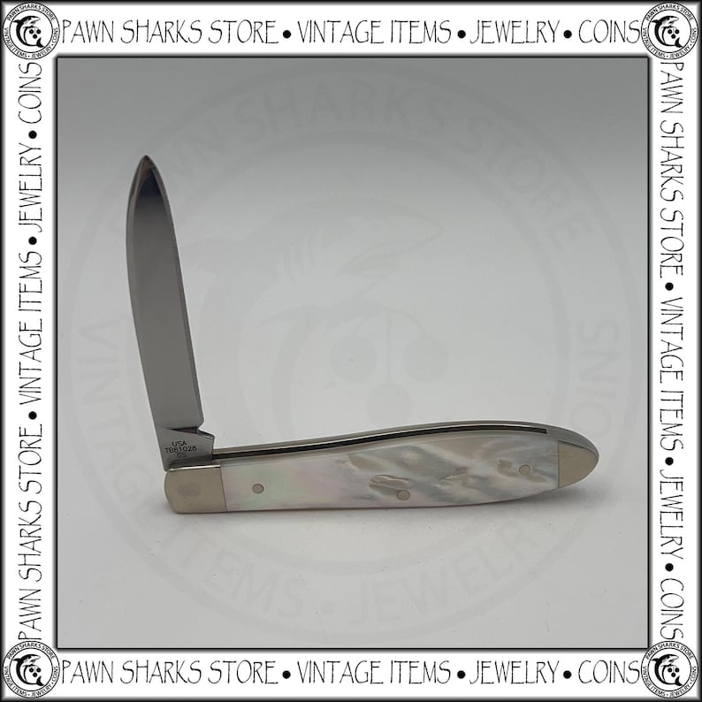 May include: A folding pocket knife with a single silver-toned blade and a handle featuring a pearlescent white finish. The base of the blade is stamped with the text USA TB61028 SS. The knife is displayed in an open position against a neutral background.