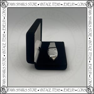 May include: A silver-toned folding pocket knife with a pearlescent handle inlay, secured by a thin black band, resting inside an open black velvet-lined display case. The knife features a metallic finish and a pointed blade tip visible in the box.