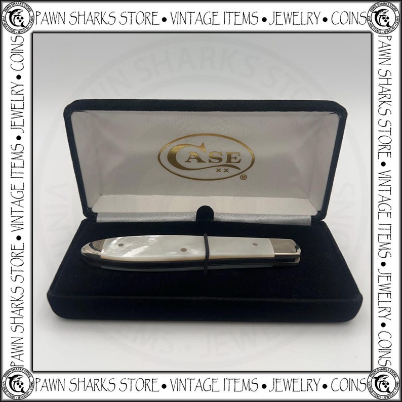 May include: A closed folding pocket knife with a white pearlescent handle and metallic bolsters, resting inside a black velvet-lined display case. The interior lid features the gold-colored text CASE XX. The case is framed by a border with text.