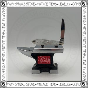 May include: A folding pocket knife with a white pearlescent handle and a single open blade, resting on a small black and silver metal anvil. The anvil features a red rectangular logo with the white text CASE TESTED XX on its side.