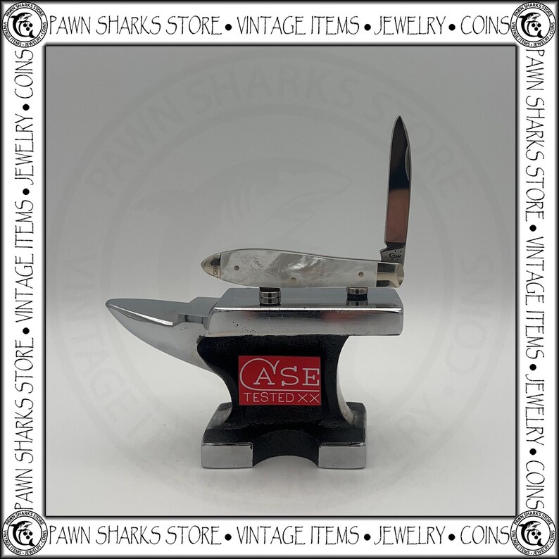 May include: A folding pocket knife with a white pearlescent handle and a single open blade, resting on a small black and silver metal anvil. The anvil features a red rectangular logo with the white text CASE TESTED XX on its side.