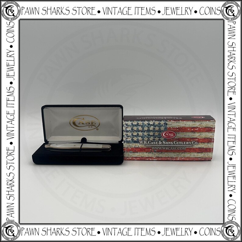 May include: A W.R. Case & Sons Cutlery Co. pocket knife with a white handle rests inside a black velvet-lined display case. Beside it sits a rectangular cardboard box featuring a distressed American flag print and the text W.R. CASE & SONS CUTLERY CO.