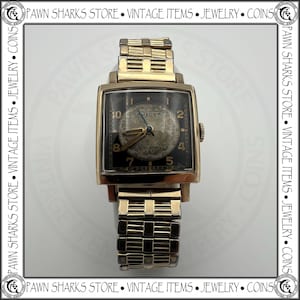 May include: Vintage Bulova watch with a rectangular gold-tone case and a black dial. The watch features gold hands and hour markers, with the Bulova logo visible. The watch band is also gold-toned, with a linked design. A classic timepiece.