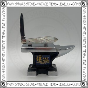 May include: A folding pocket knife with a pearlescent handle and a single upright blade resting on a small, polished metal anvil. The anvil features a blue rectangular label with the text Case, Tested XX, Manufacturers of Quality Cutlery, Bradford, PA.