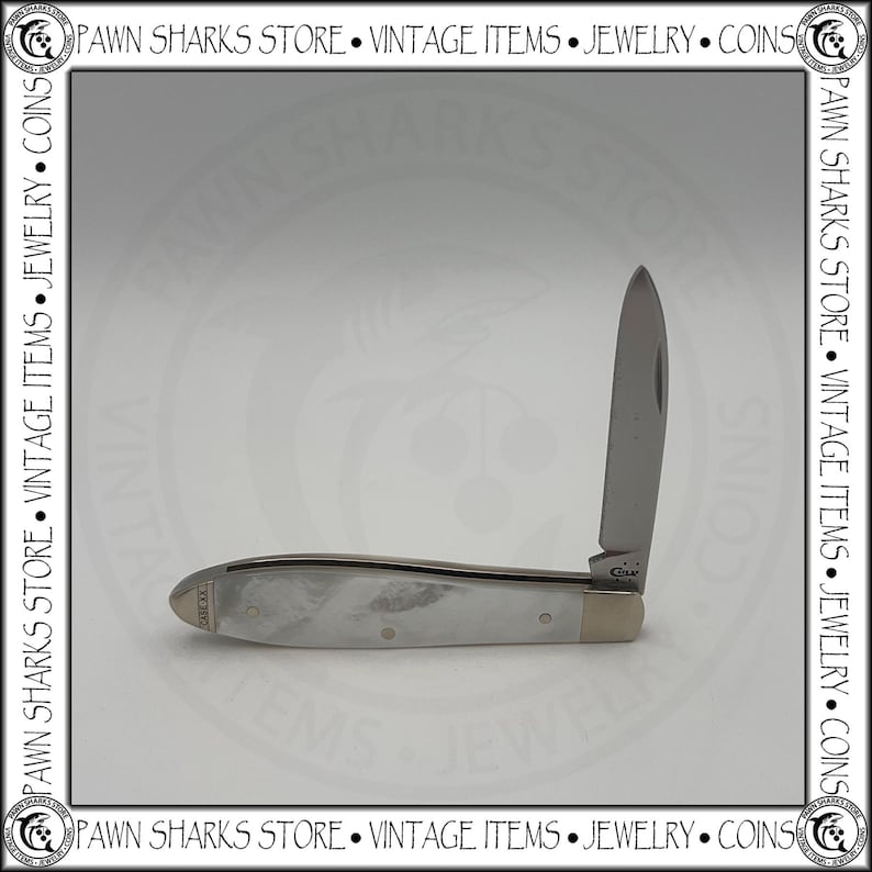 May include: A folding pocket knife with a single silver-toned blade and a handle featuring a pearlescent white marbled finish. The handle includes a metallic bolster and a small metal inlay at the end marked with the text XX 1889.
