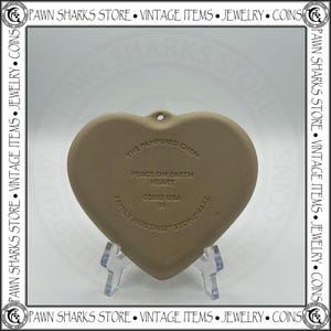 K&ouml;nnte beinhalten: Herzf&ouml;rmiger Steinzeug-Ornament von The Pampered Chef mit dem Text "Peace on Earth Heart" und dem Jahr 2002. Das Ornament ist hellbraun und hat ein Loch zum Aufh&auml;ngen. Ein Vintage-Artikel.