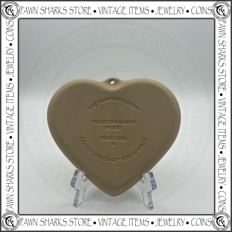 K&ouml;nnte beinhalten: Herzf&ouml;rmiger Steinzeug-Ornament von The Pampered Chef mit dem Text "Peace on Earth Heart" und dem Jahr 2002. Das Ornament ist hellbraun und hat ein Loch zum Aufh&auml;ngen. Ein Vintage-Artikel.