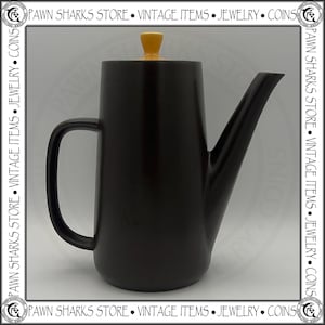 May include: A black ceramic coffee pot with a curved handle and a long spout. The lid is yellow. The pot is a vintage item. The Pawn Sharks Store logo is in the border.