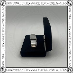 May include: A small folding pocket knife with a smooth, light-colored handle and a metallic bolster, resting inside a dark blue velvet-lined display case. The case is open, revealing the knife positioned horizontally against the dark fabric interior.