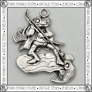 May include: A silver-toned charm depicting a frog fishing. The frog, wearing a coat and hat, stands on a cloud-like base, holding a fishing rod and net. A fish is hooked on the line. The charm has a loop for attachment.