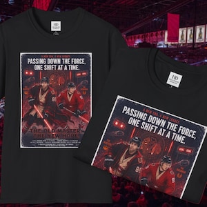 Op de afbeelding: Twee zwarte t-shirts met korte mouwen en een grafische print van twee ijshockeyspelers in rood-zwarte shirts die lichtzwaarden vasthouden. De tekst luidt: A NEW ERA. A NEW LEGACY. PASSING DOWN THE FORCE, ONE SHIFT AT A TIME. THE OLD MASTER THE NEW HOPE.