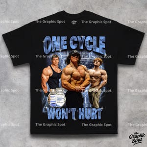 Flat lay of black t-shirt showing full graphic design reading One Cycle Wont Hurt with three illustrated bodybuilders and a supplement bottle, The Graphic Spot brand tee