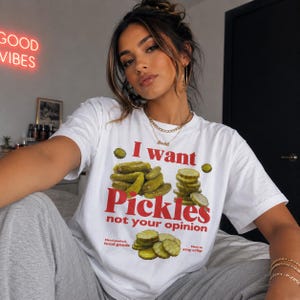 May include: White t-shirt with the text "I want Pickles not your opinion" in red. The shirt features a graphic of pickles and the phrases "Hand packed, local goods" and "Made to stay crisp".