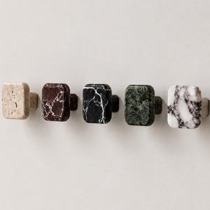 Peut inclure: Un ensemble de cinq boutons de placard rectangulaires en pierre naturelle. Les boutons présentent des motifs et des couleurs distincts, notamment du travertin beige, du marbre brun foncé, du marbre noir veiné de blanc, du marbre vert foncé et du marbre blanc veiné.