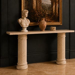 May include: A console table featuring a long, rectangular top supported by two fluted, column-style legs. On the table sits a white bust of a person, a brown ceramic vase, and a small, textured, cylindrical object, all placed before a framed painting.